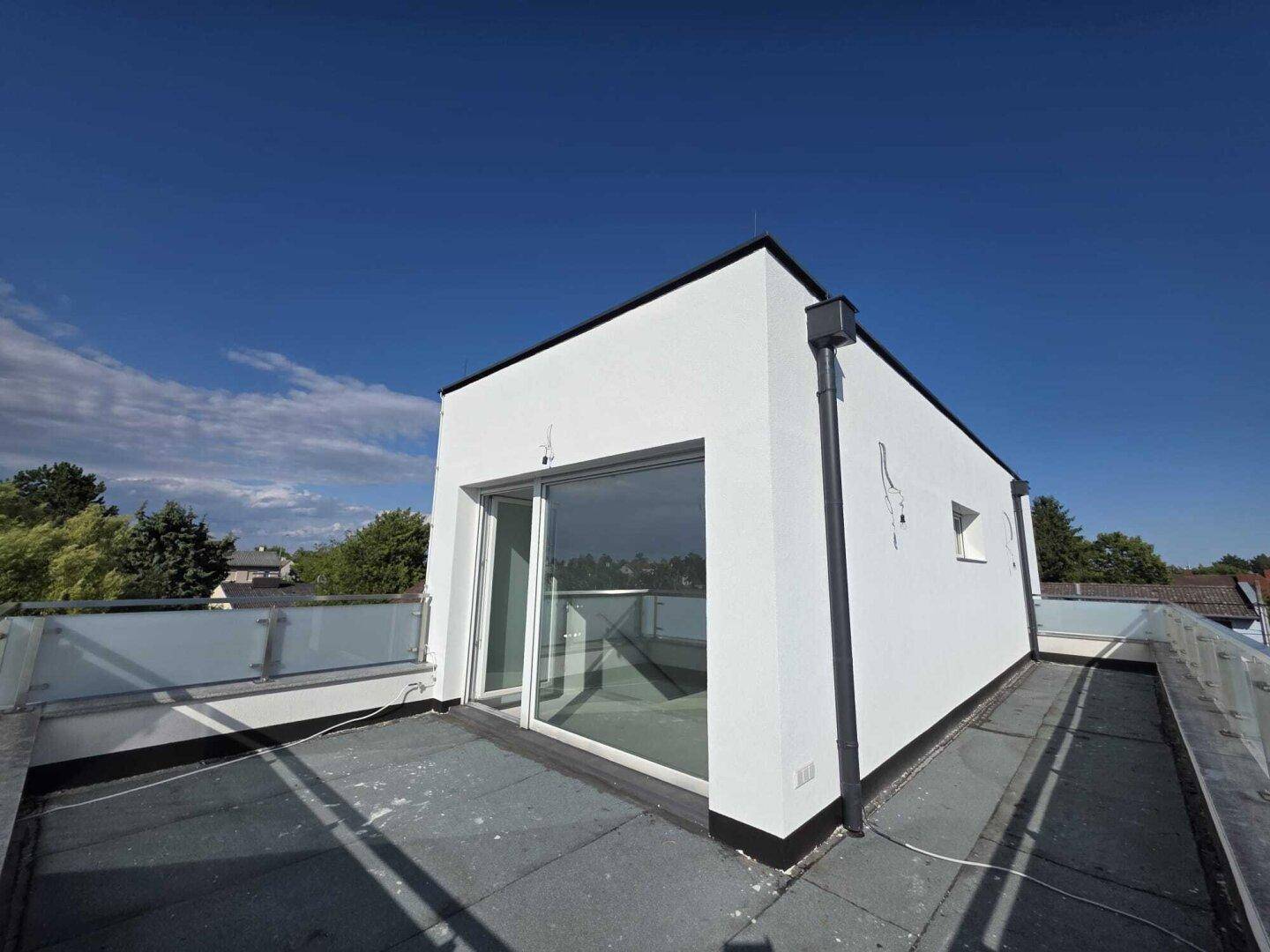 Dachterrasse des modernen Neubaus mit Glasgeländer und weitem Blick in die Landschaft.