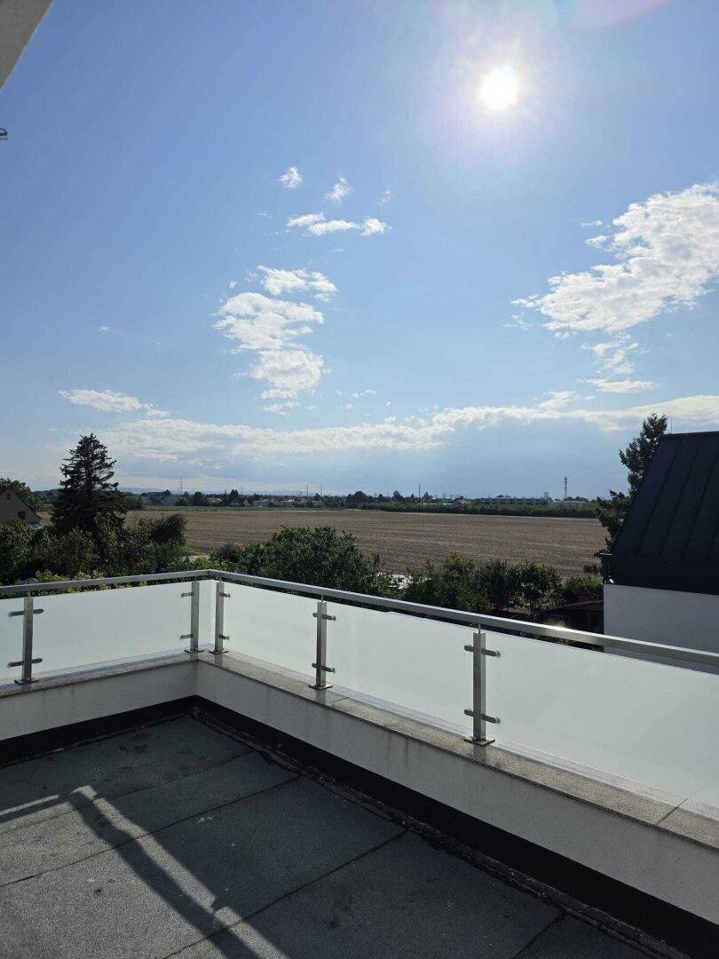 Sonnige Dachterrasse mit Glasgeländer und weitem Blick über Felder und Landschaft.