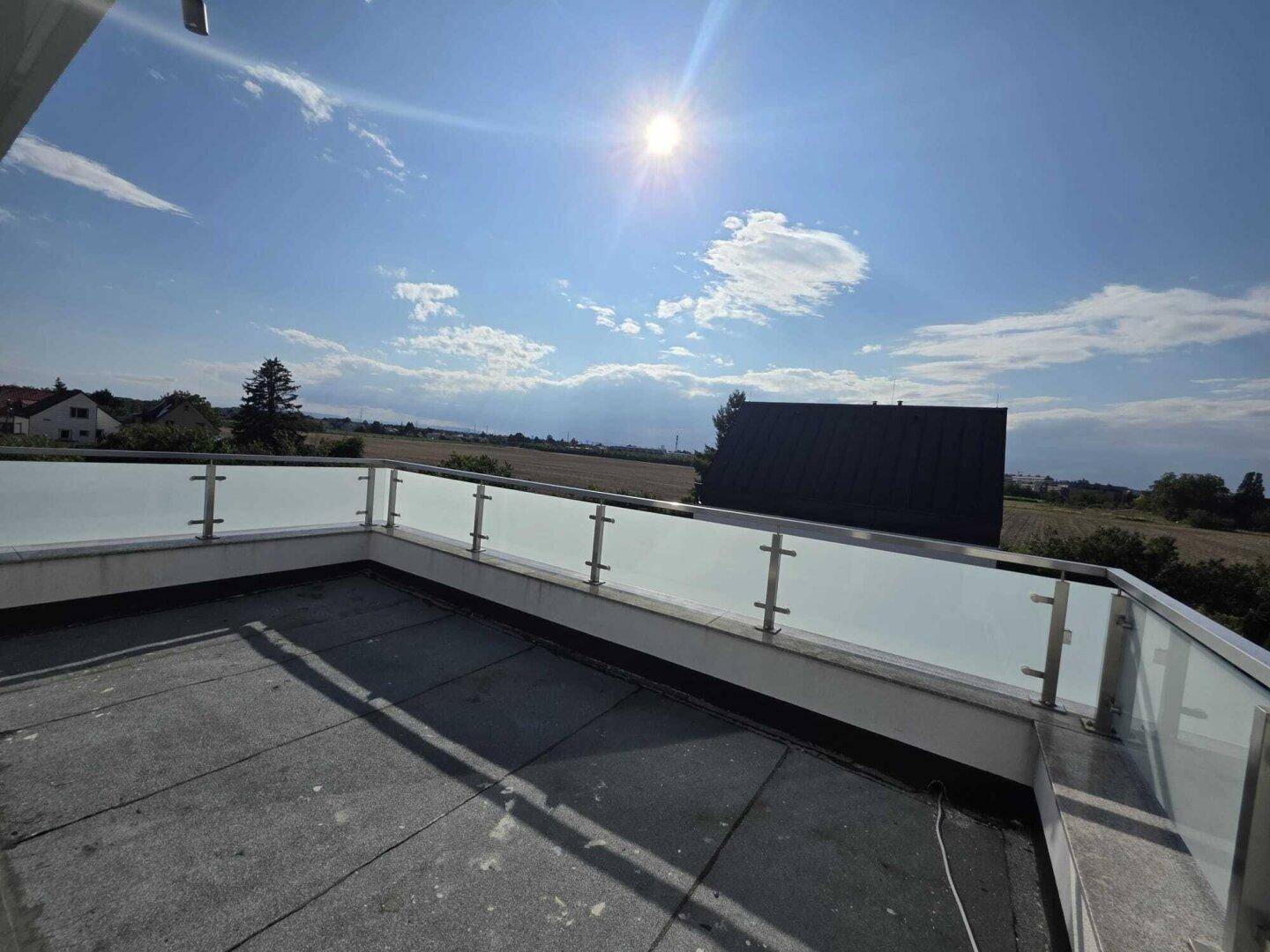 Sonnige Dachterrasse mit Glasgeländer und weitem Blick über Felder und Landschaft.