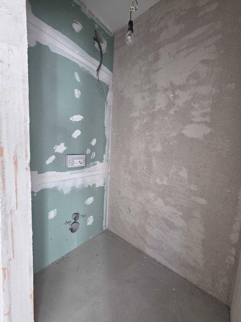 Unfertiges Badezimmer mit vorbereiteten Anschlüssen und Trockenbauwänden für den Ausbau.