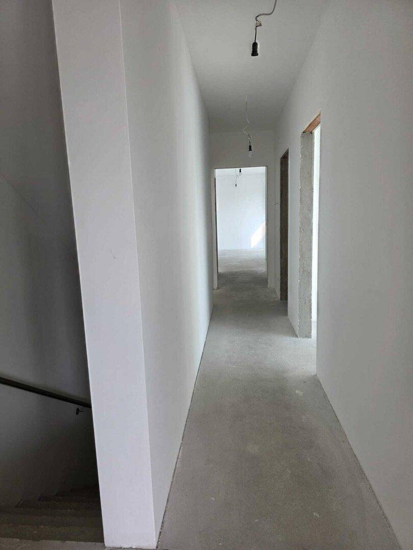 Langer, heller Flur in einem unfertigen Neubau mit Rohbetonboden und weißen Wänden.