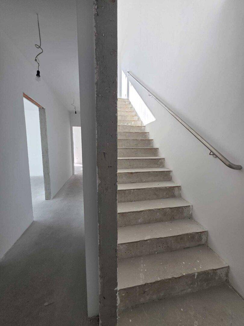 Heller Treppenaufgang und Flur in einem unfertigen Neubau mit Betonstufen und Geländer.