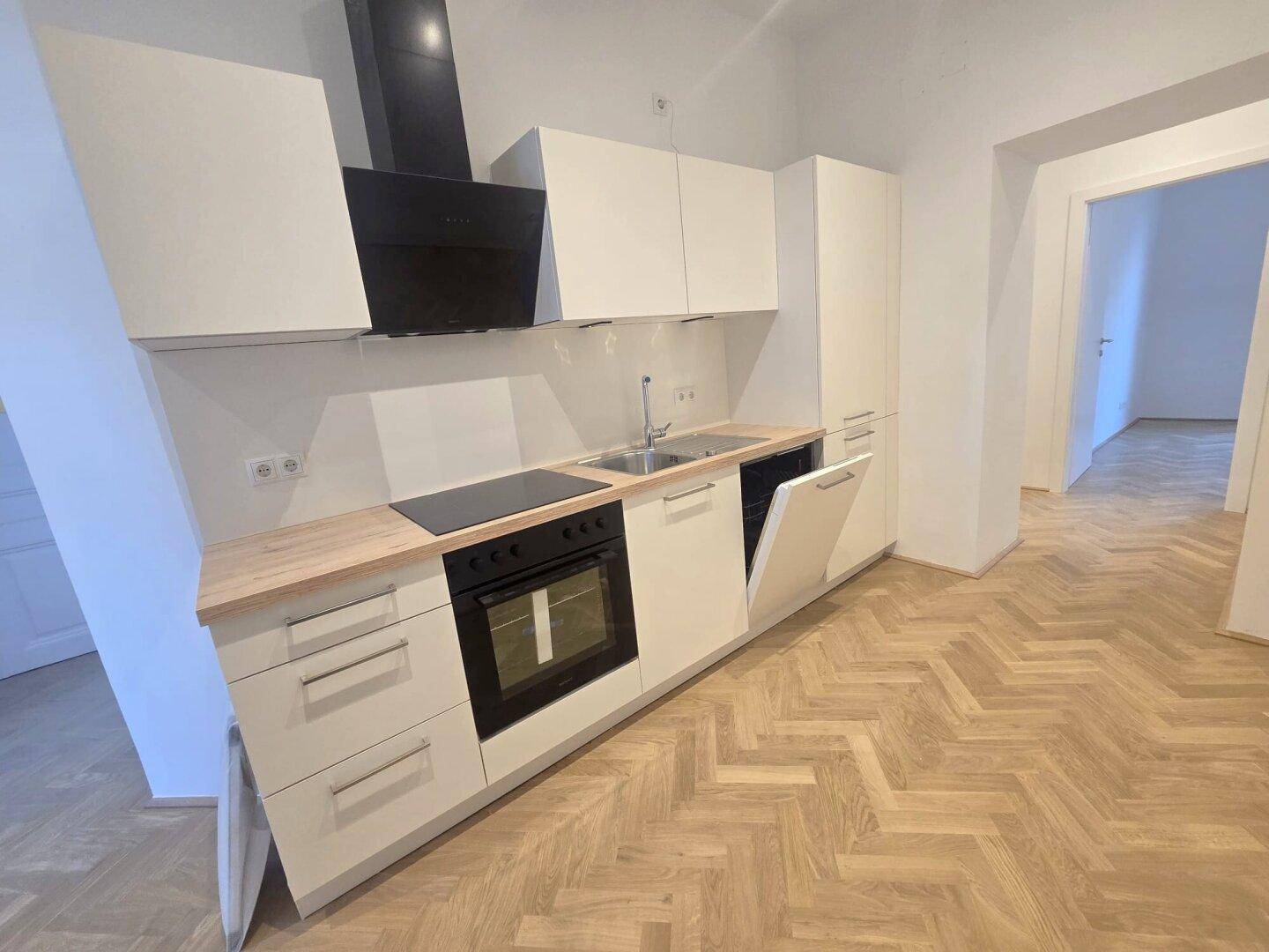 Moderne Einbauküche mit weißen Schränken, Holz-Arbeitsplatte und neuen Geräten, inklusive Geschirrspüler und Ofen.