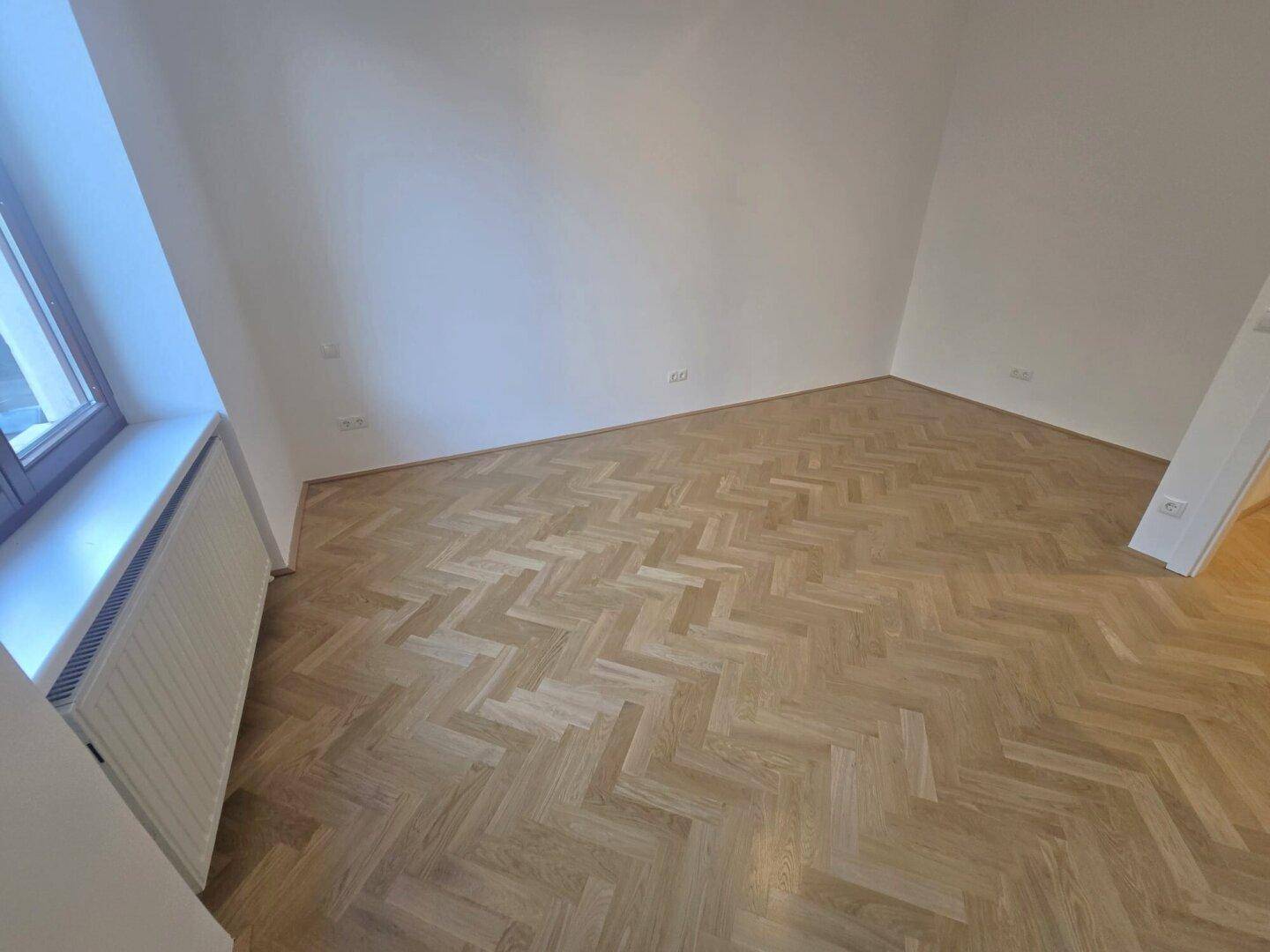 Helles Schlafzimmer mit neuem Fischgrätparkett und weißen Wänden, bereit zur individuellen Gestaltung.
