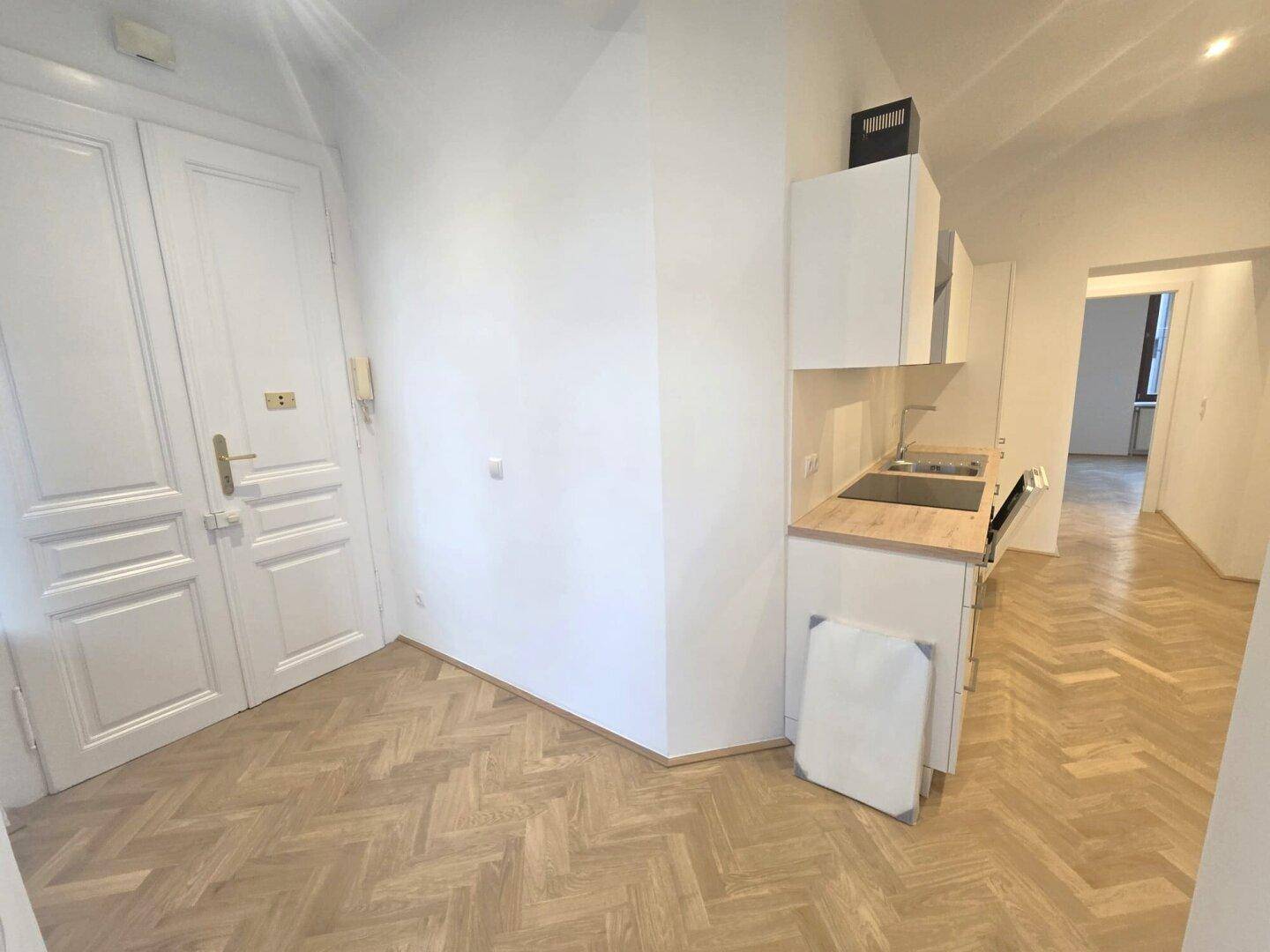 Heller Raum mit Fischgrätparkett und einer kompakten Küchenzeile, ideal für kleine Wohnbereiche.