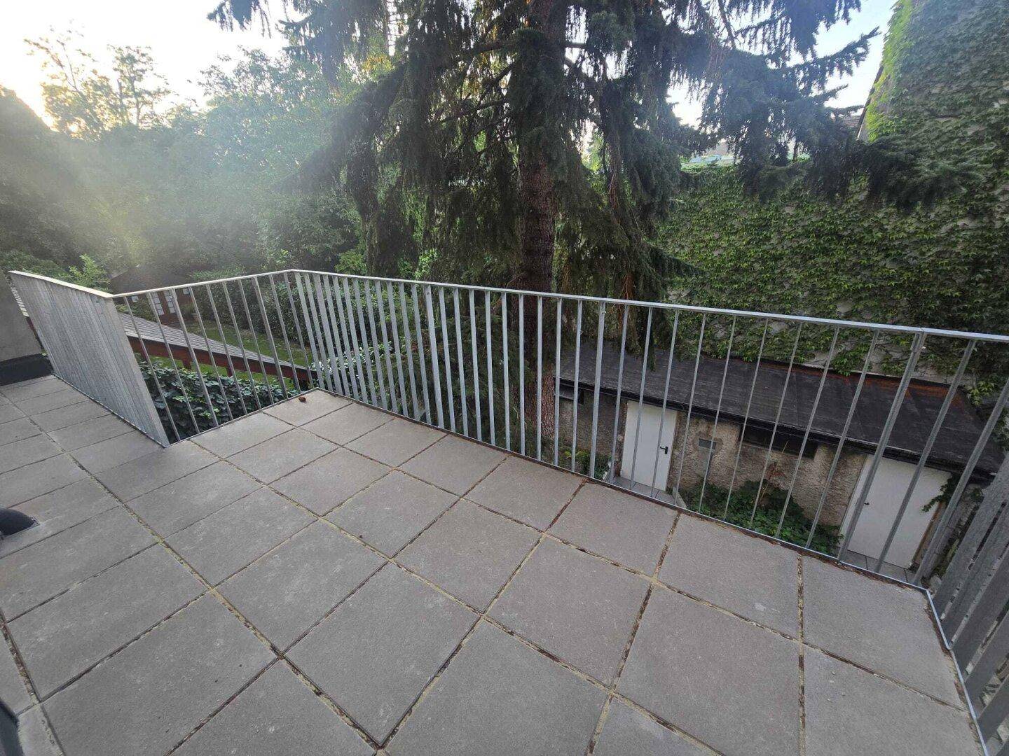 Weitläufige Terrasse mit Blick auf üppiges Grün und angrenzende Gebäude, perfekt zum Entspannen.