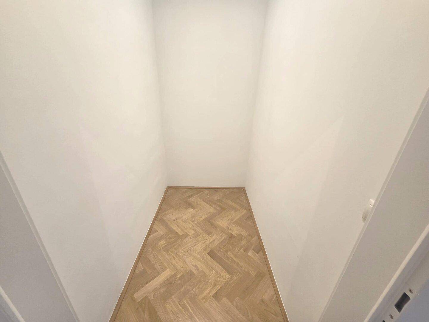 Kleiner, schmaler Raum mit Fischgrätparkett und weißen Wänden, ideal als Abstellraum oder begehbarer Schrank.