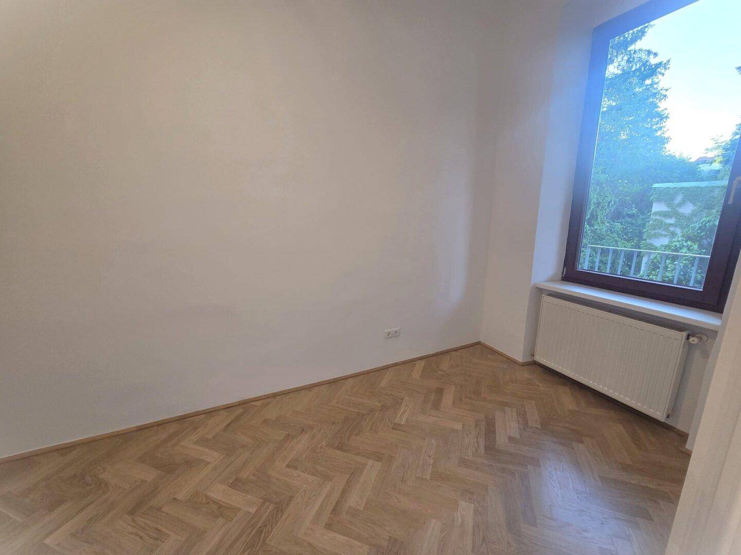 Ruhiges Zimmer mit Fischgrätparkett und einem Fenster mit Blick ins Grüne, ideal als Schlafzimmer.
