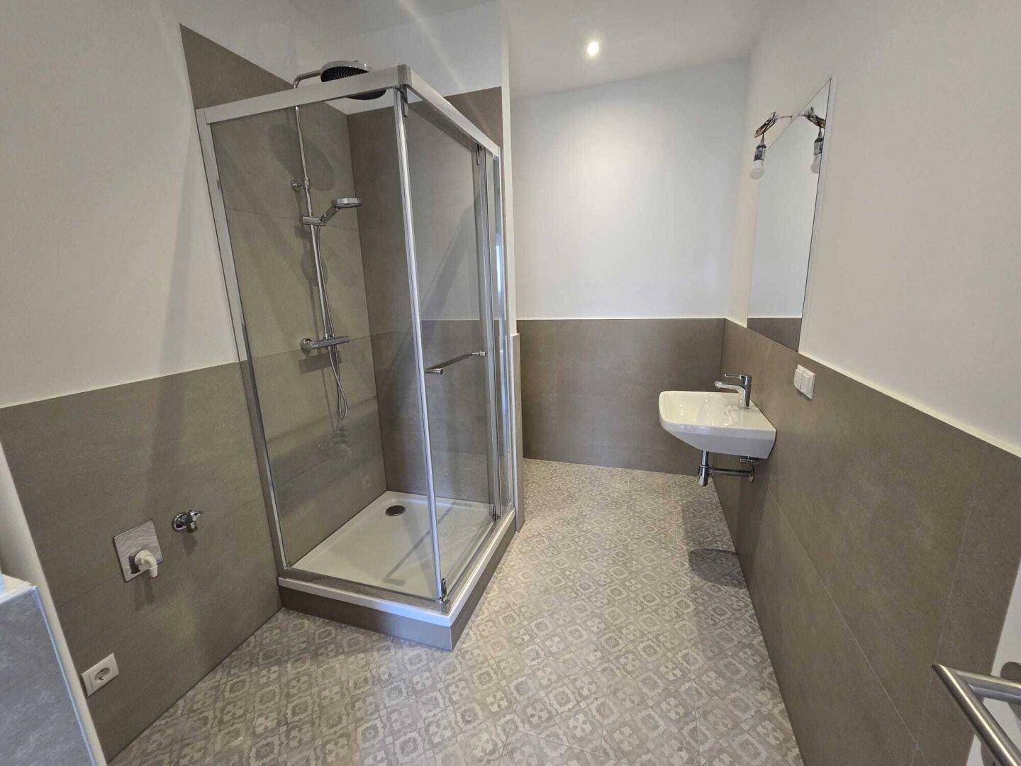 Modernes Badezimmer mit Duschkabine, wandhängendem Waschbecken und gemusterten grauen Fliesen.