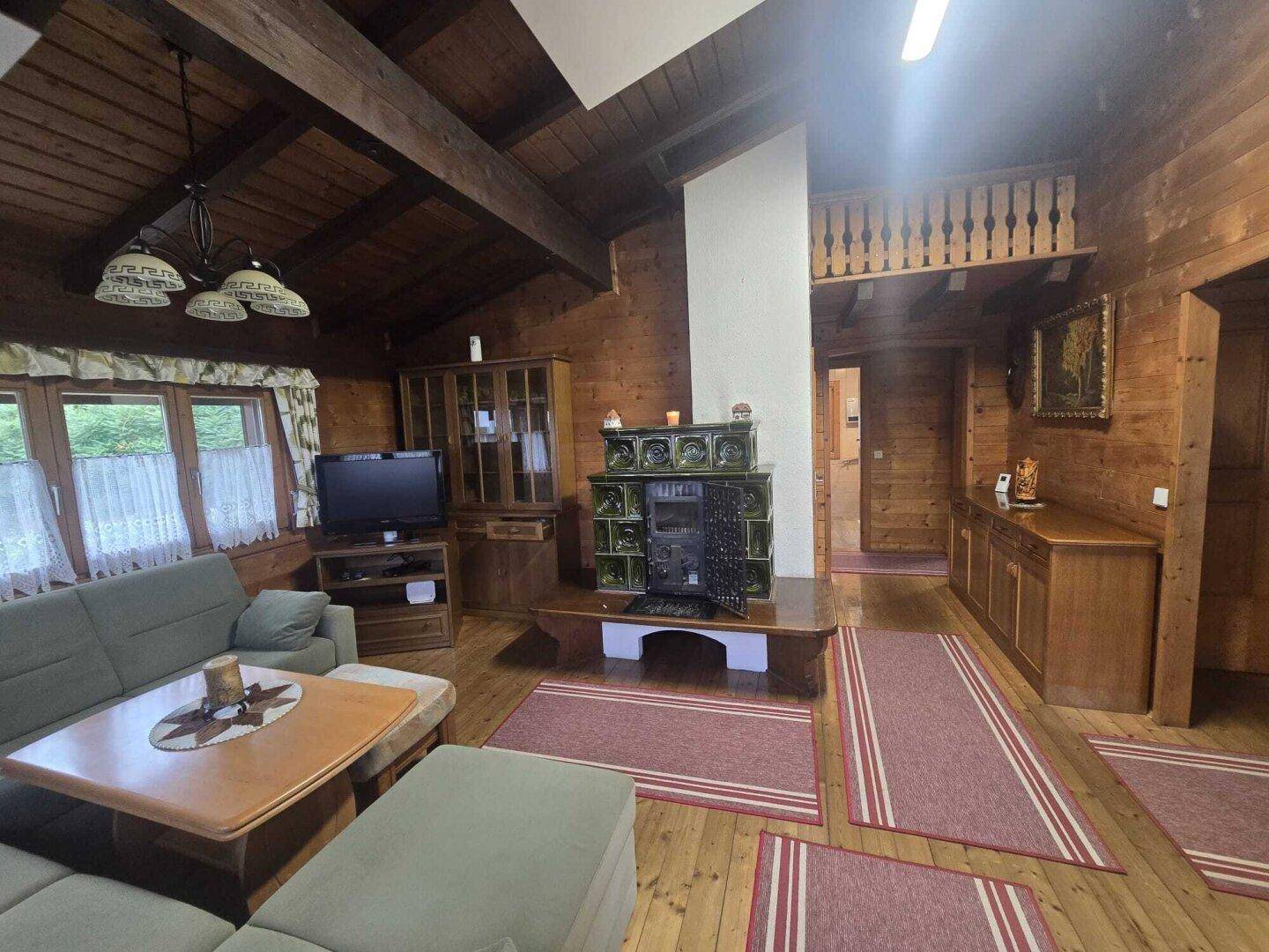 Rustikales Wohnzimmer mit Holzwänden, Holzbalkendecke und einem traditionellen Kachelofen.