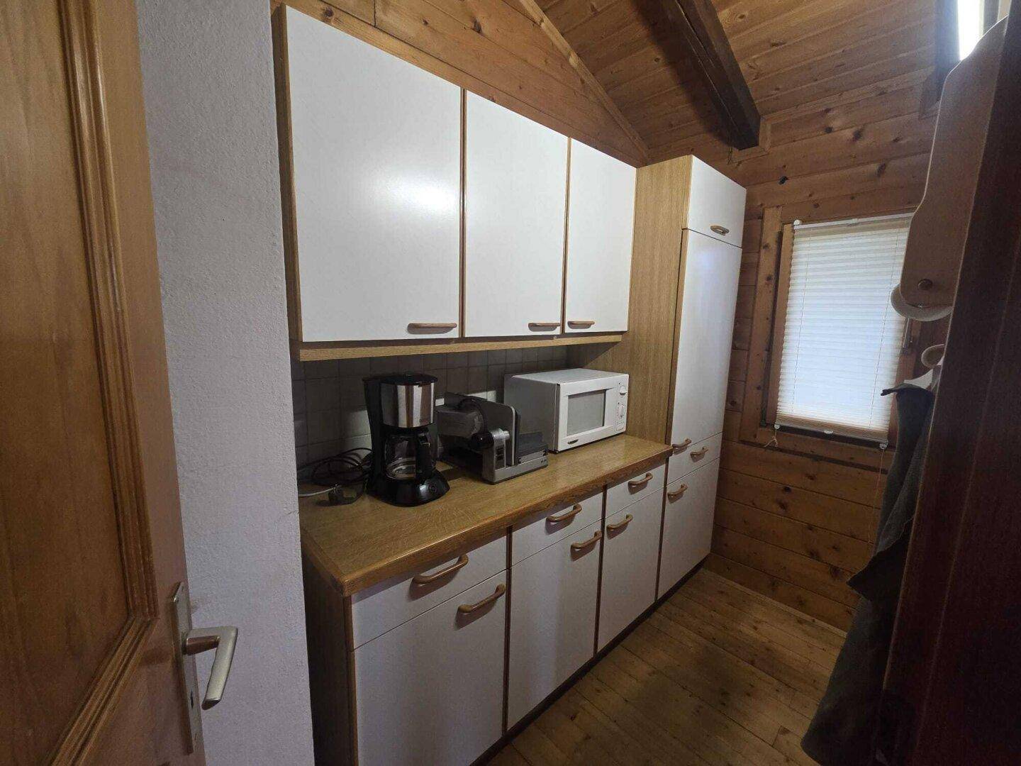 Kleine Küchenzeile mit Kaffeemaschine, Mikrowelle und weißen Schränken.