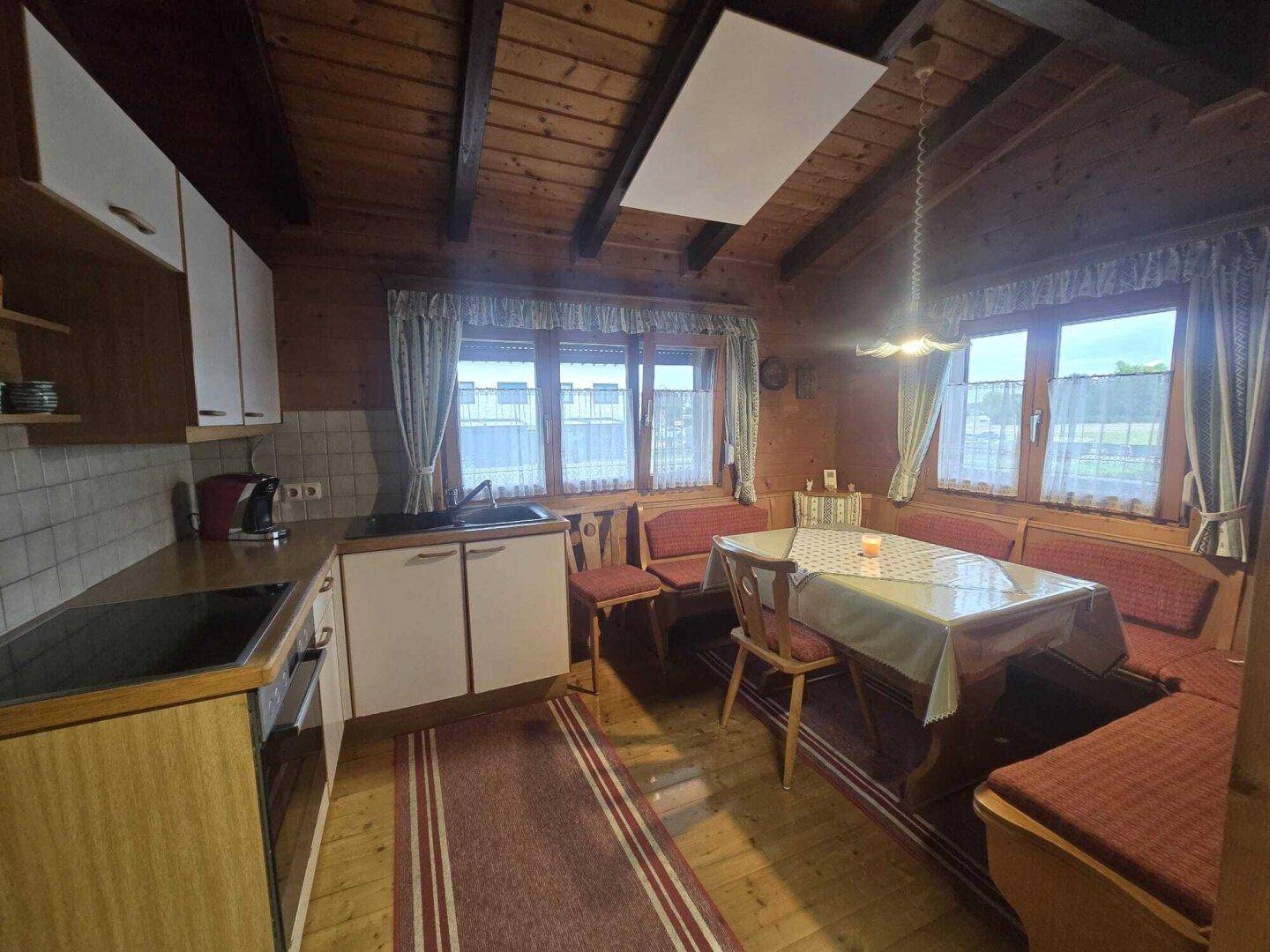 Gemütliche Wohnküche im Landhausstil mit Holzwänden, Essbereich und kleinen Fenstern.