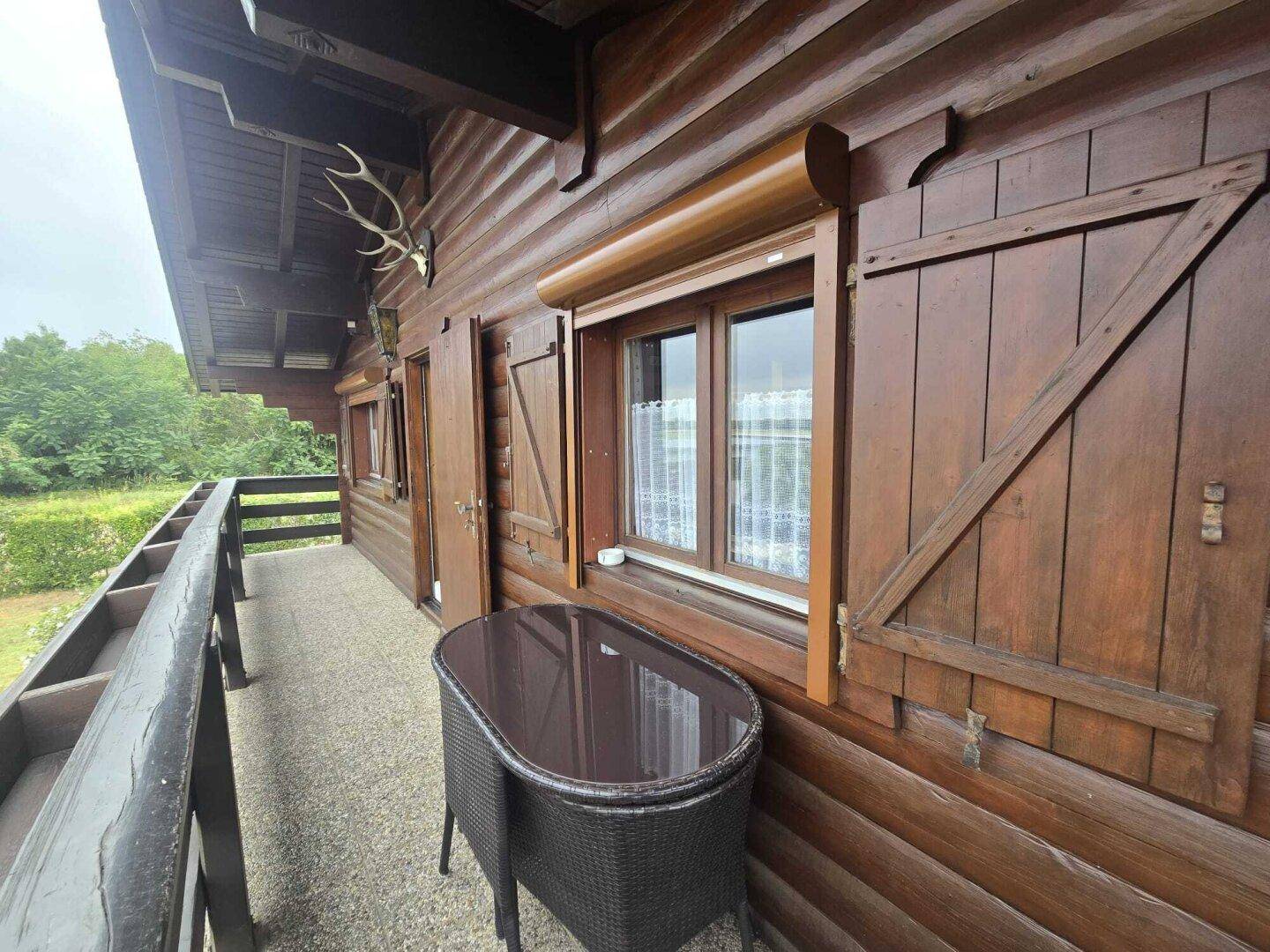 Gemütlicher Balkon mit Holzboden, kleinem Tisch und Blick ins Grüne.