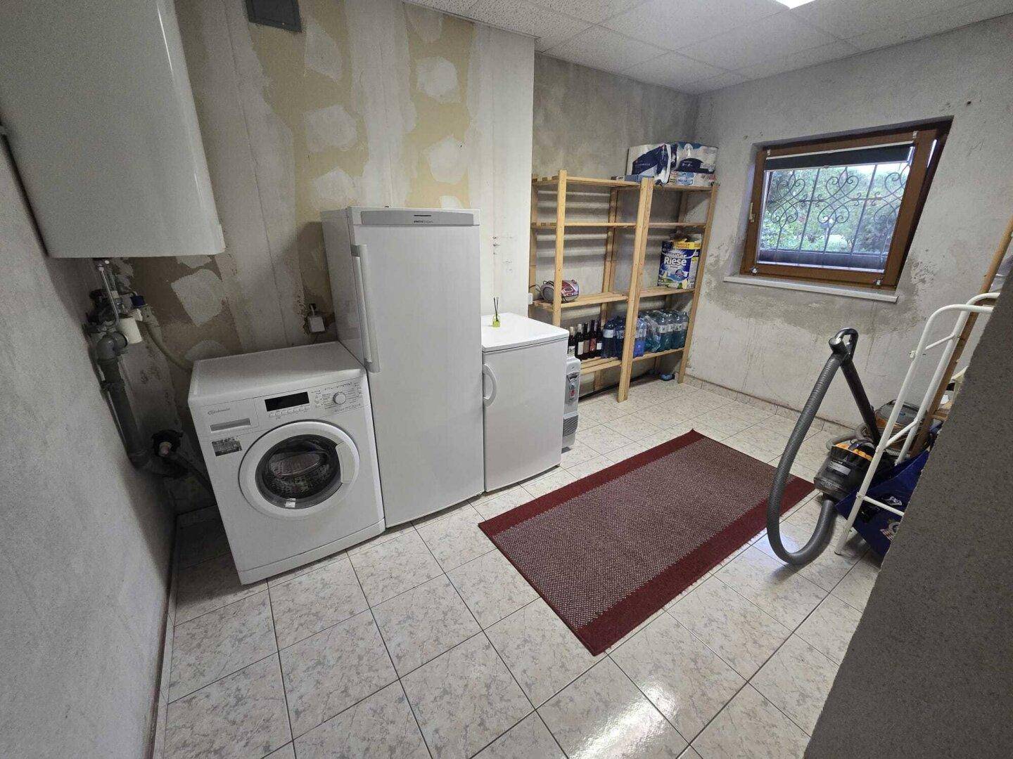 Praktischer Hauswirtschaftsraum mit Waschmaschine, Kühlschrank und Regalen für Vorräte.