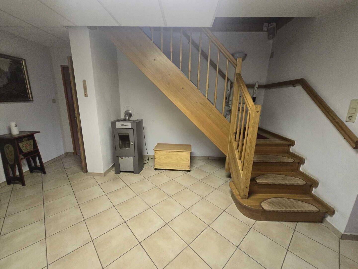 Geräumiger Flur mit Holztreppe, Fliesenboden und einem gemütlichen Holzofen.