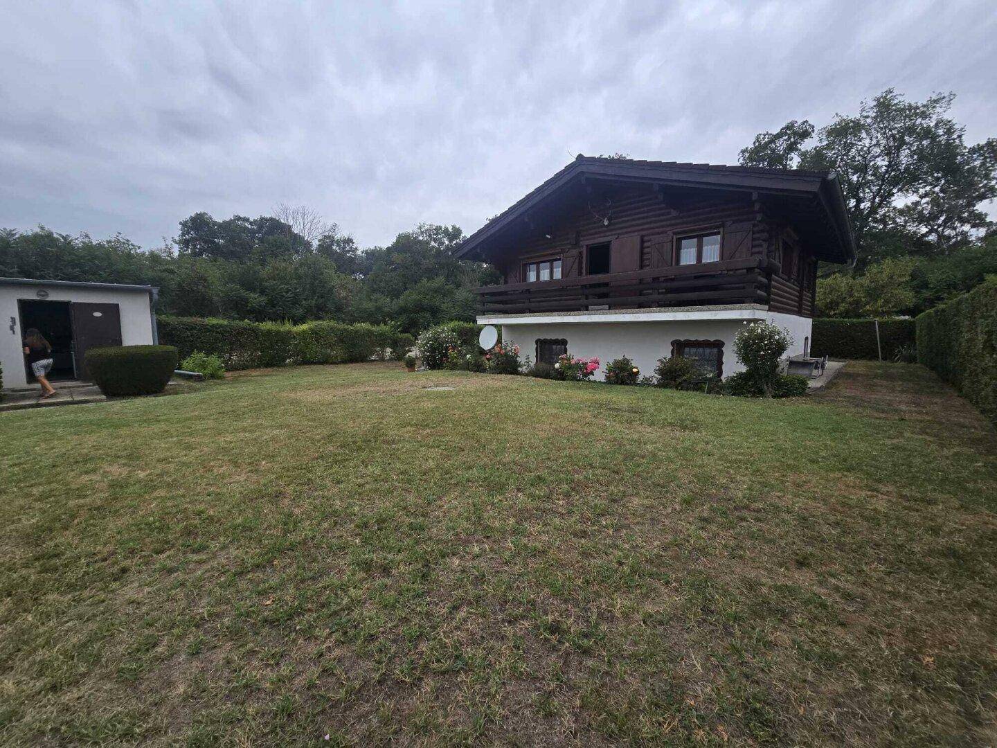 Rustikales Holzhaus mit großem Rasenbereich und gepflegten Hecken im Garten.