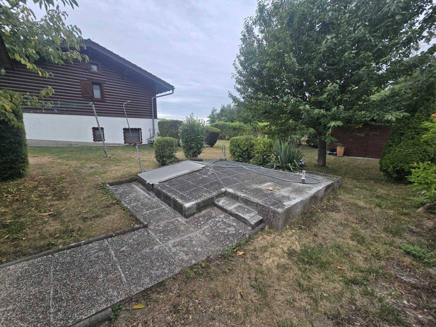 Gartenbereich neben dem Haus mit einer alten Betonstruktur und Rasenfläche.