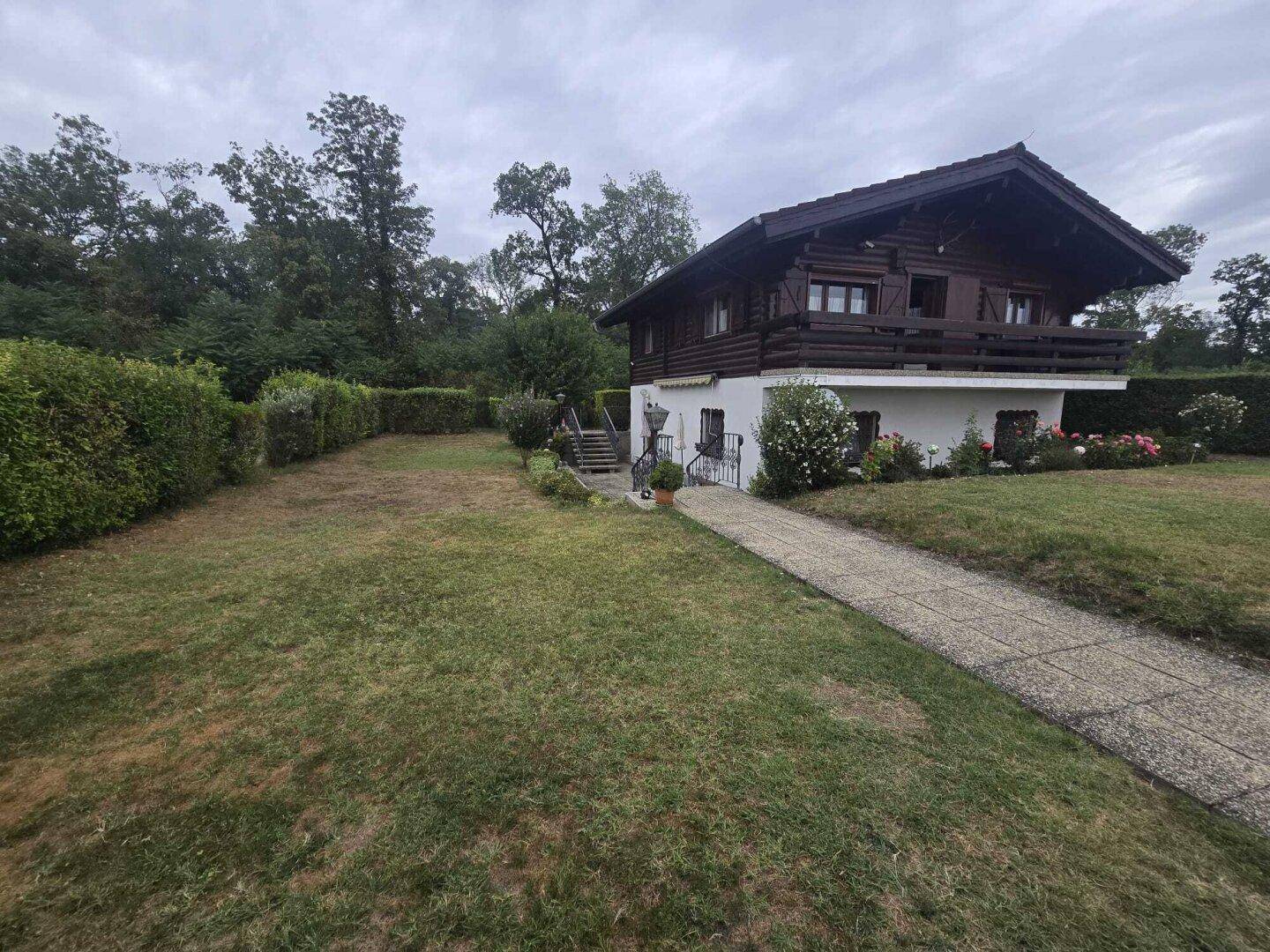 Seitenansicht des Holzhauses mit gepflegtem Garten, Rasenfläche und einem Steinweg.