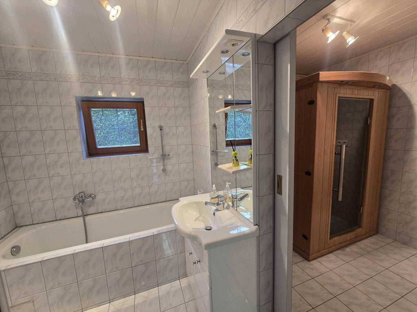 Badezimmer mit Badewanne, Waschbecken, Spiegelschrank und einer integrierten Sauna.