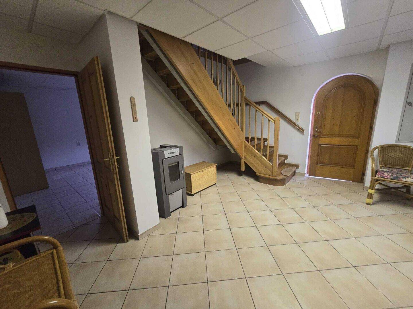 Heller Eingangsbereich mit Holztreppe, Fliesenboden und einem modernen Holzofen.