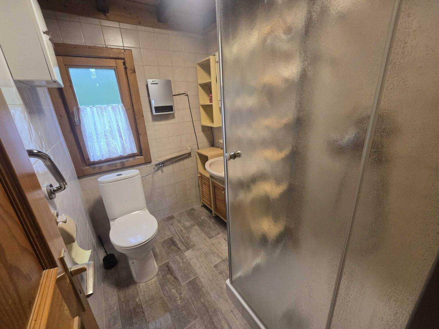 Kleines Badezimmer mit Dusche, Toilette, Waschbecken und Fliesenboden.