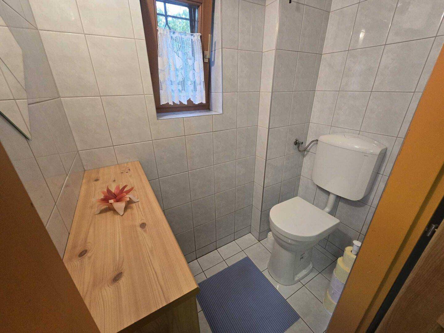 Separates WC mit Toilette, kleinem Fenster und einer Holzablage.