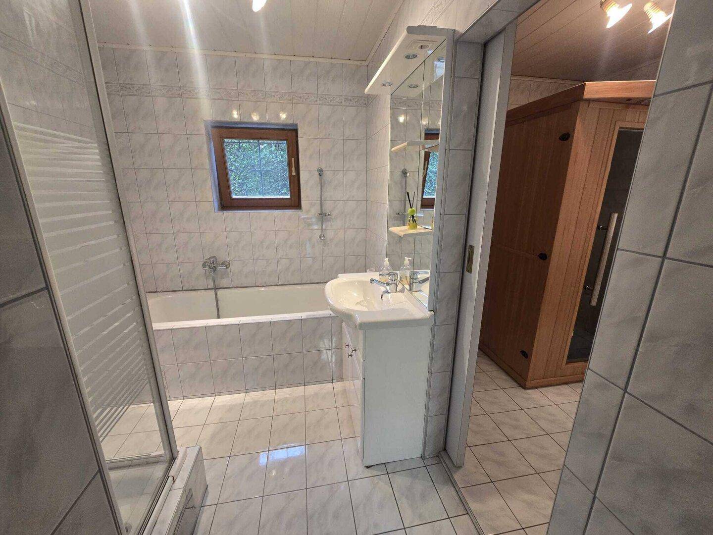 Geräumiges Badezimmer mit Badewanne, Duschbereich und einer modernen Saunakabine.