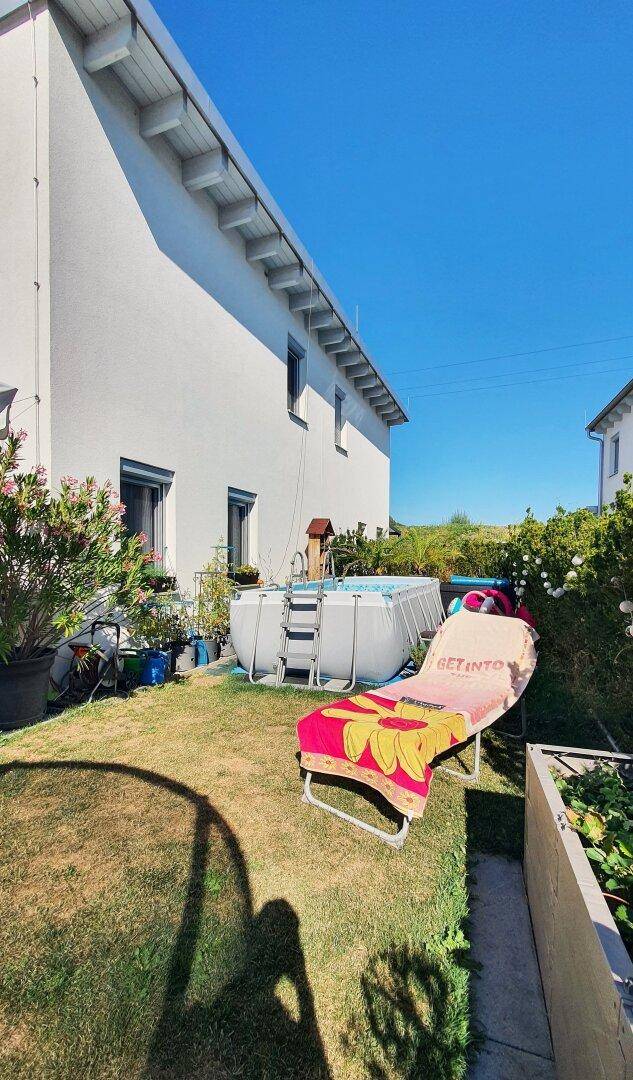 Hinterhof mit aufstellbarem Pool, Liegestuhl und grüner Rasenfläche an sonnigem Tag.