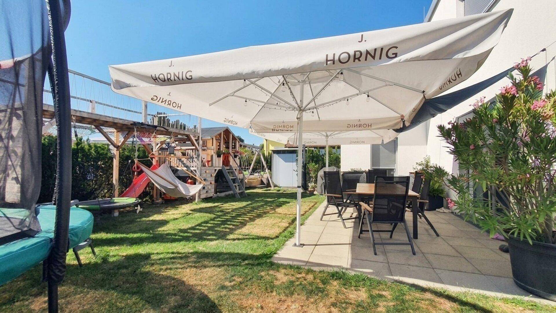 Sonniger Garten mit Terrasse, Sitzbereich und Spielgeräten für Kinder.