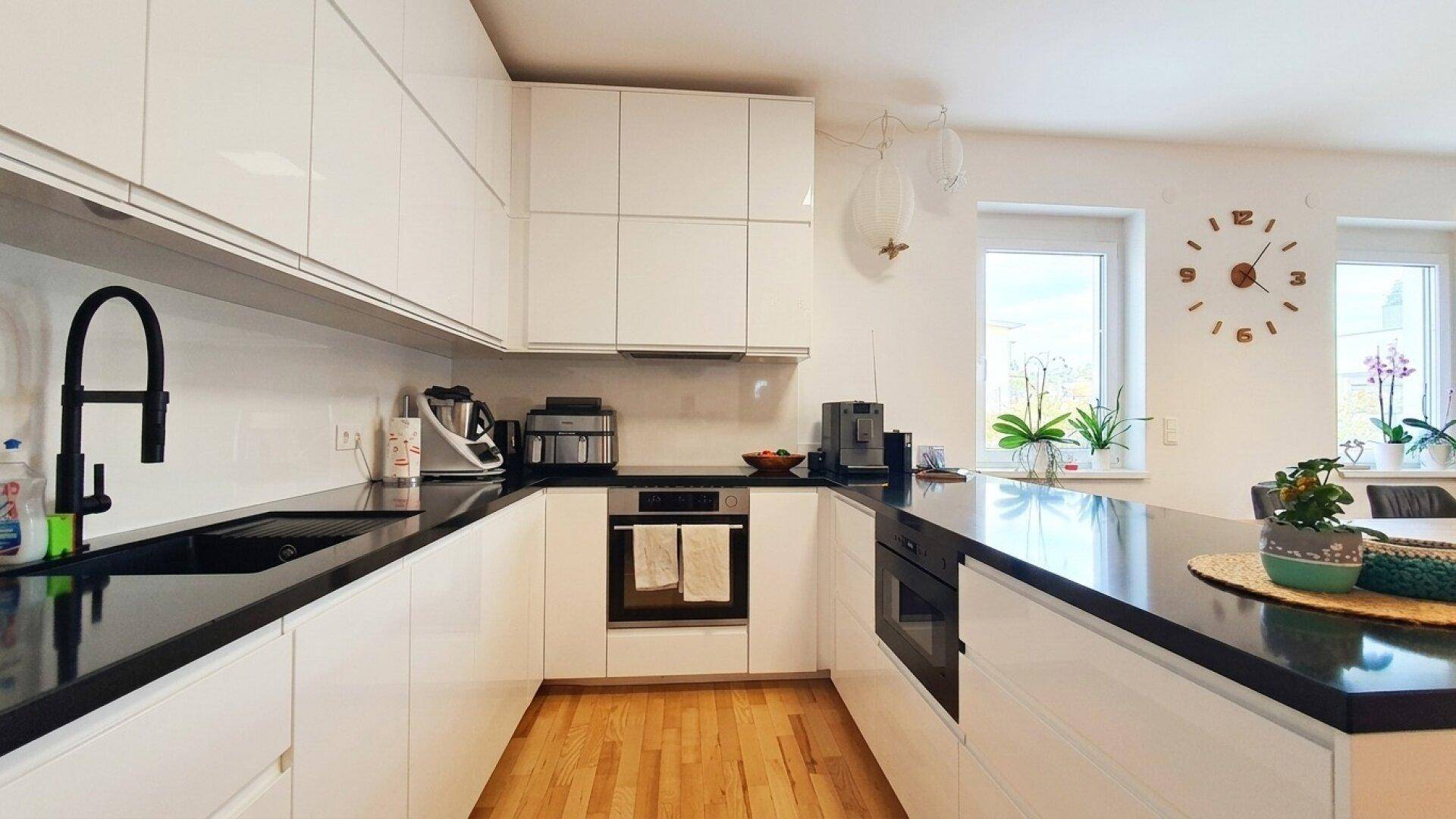 Moderne Küche mit weißen Hochglanzfronten, schwarzen Arbeitsplatten und integrierten Geräten.