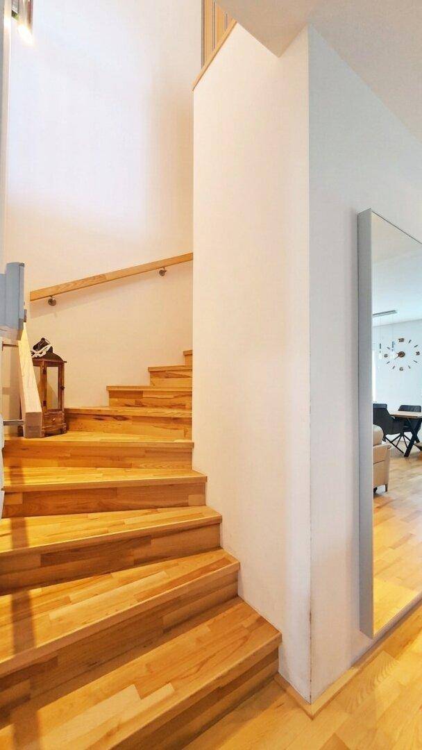 Moderne Holztreppe mit hellem Geländer und Spiegel im Flurbereich.