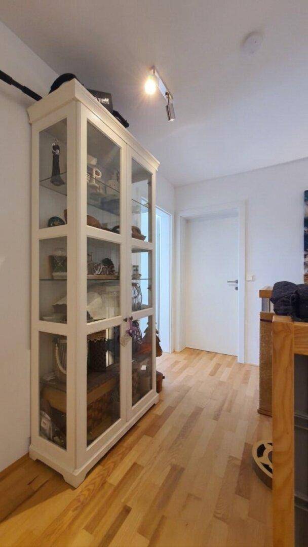 Flur mit weißer Vitrine und Holzboden, der zu weiteren Räumen führt.