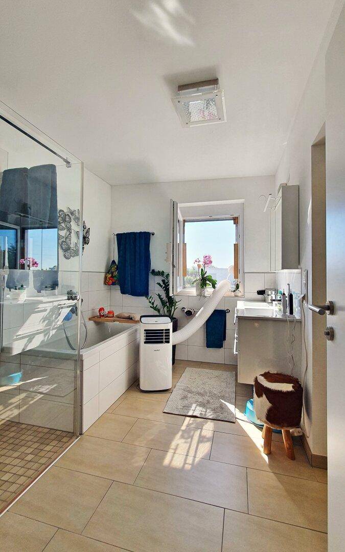 Modernes Badezimmer mit Badewanne, Dusche, Fenster und Klimaanlage.