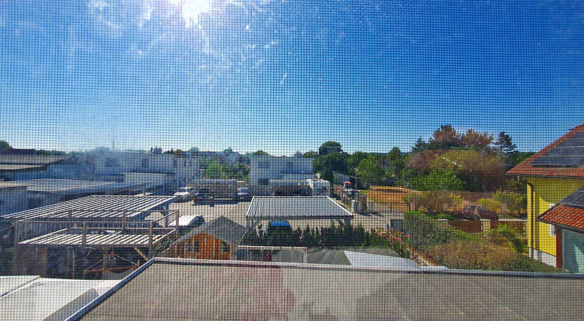 Ausblick aus dem Fenster auf ein Gewerbegebiet mit Bäumen im Hintergrund.