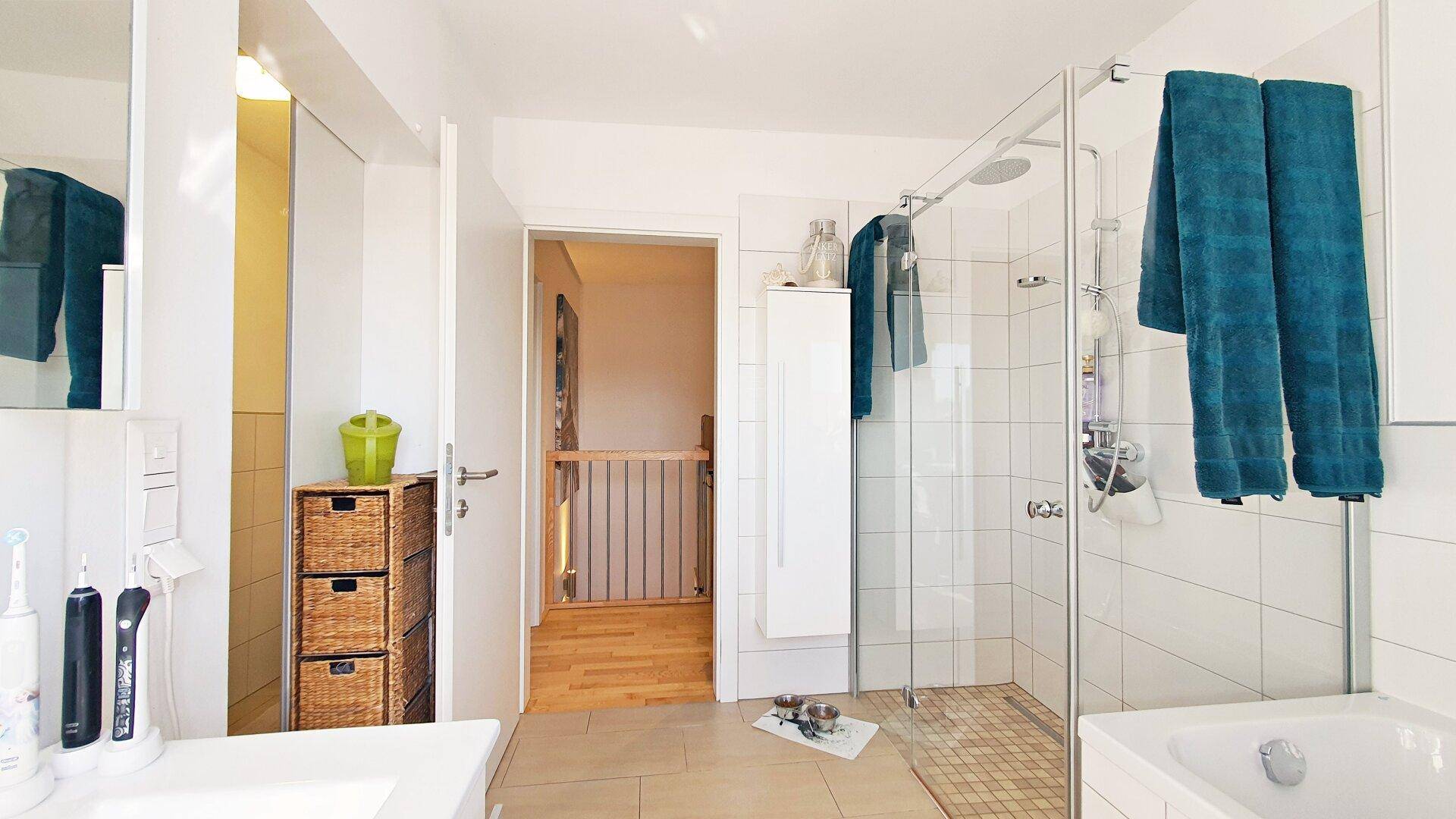 Helles Badezimmer mit Duschkabine, Einzelwaschbecken und Blick in den Flur.