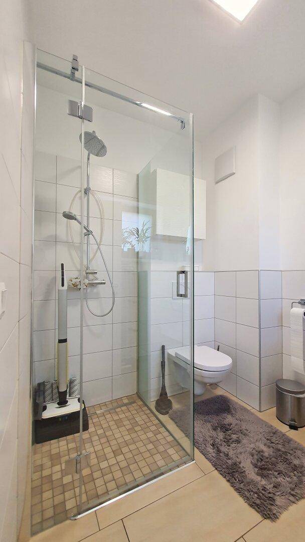 Modernes Badezimmer mit begehbarer Dusche, weißen Fliesen und WC.