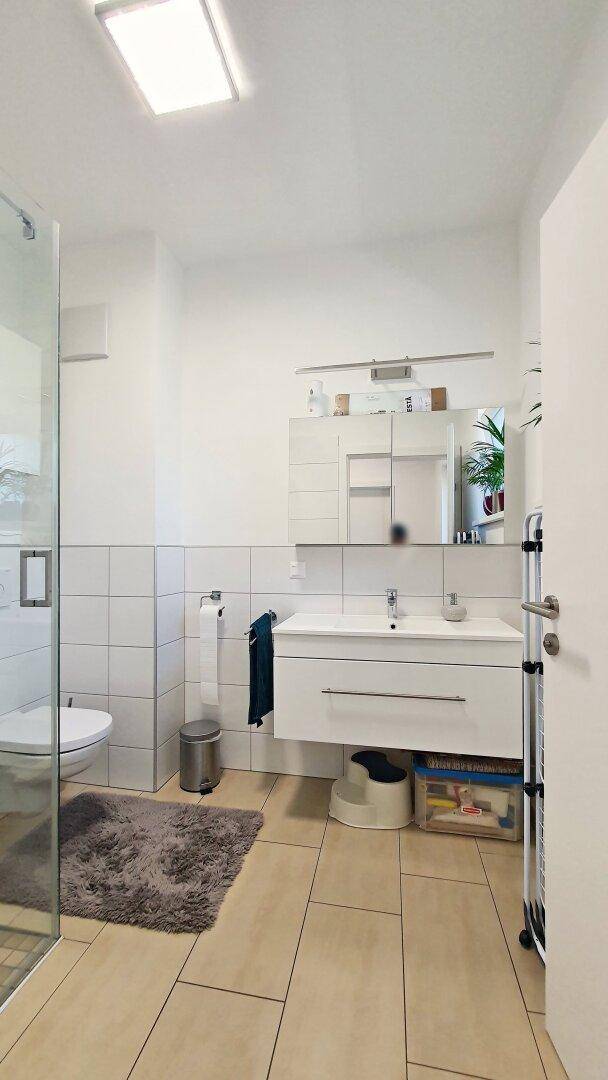 Helles Badezimmer mit Waschtisch, Spiegelschrank und begehbarer Dusche.