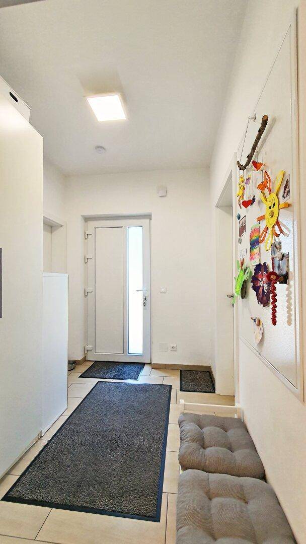 Eingangsbereich mit Fliesenboden, weißer Wand und Sitzbank.