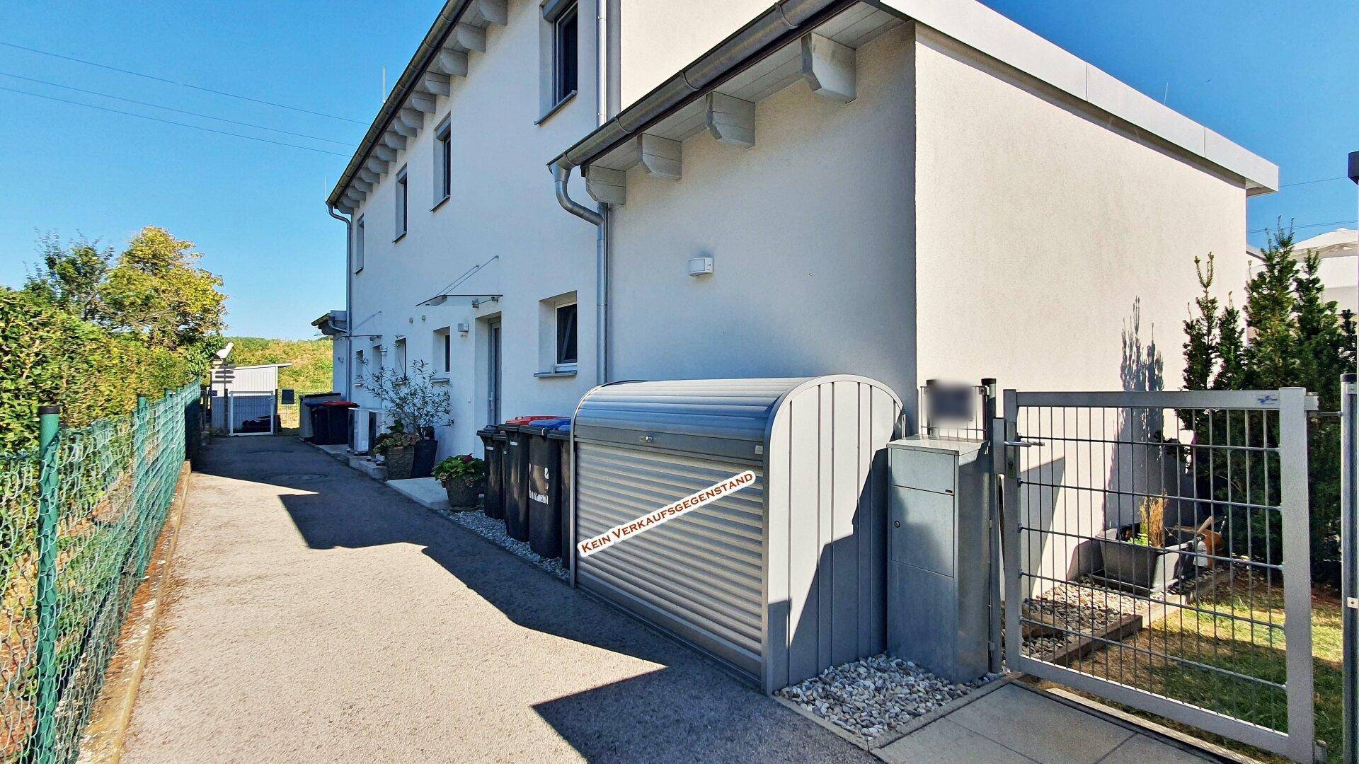 Außenansicht eines Wohnhauses mit gepflegtem Gartenbereich und Mülltonnenbox.