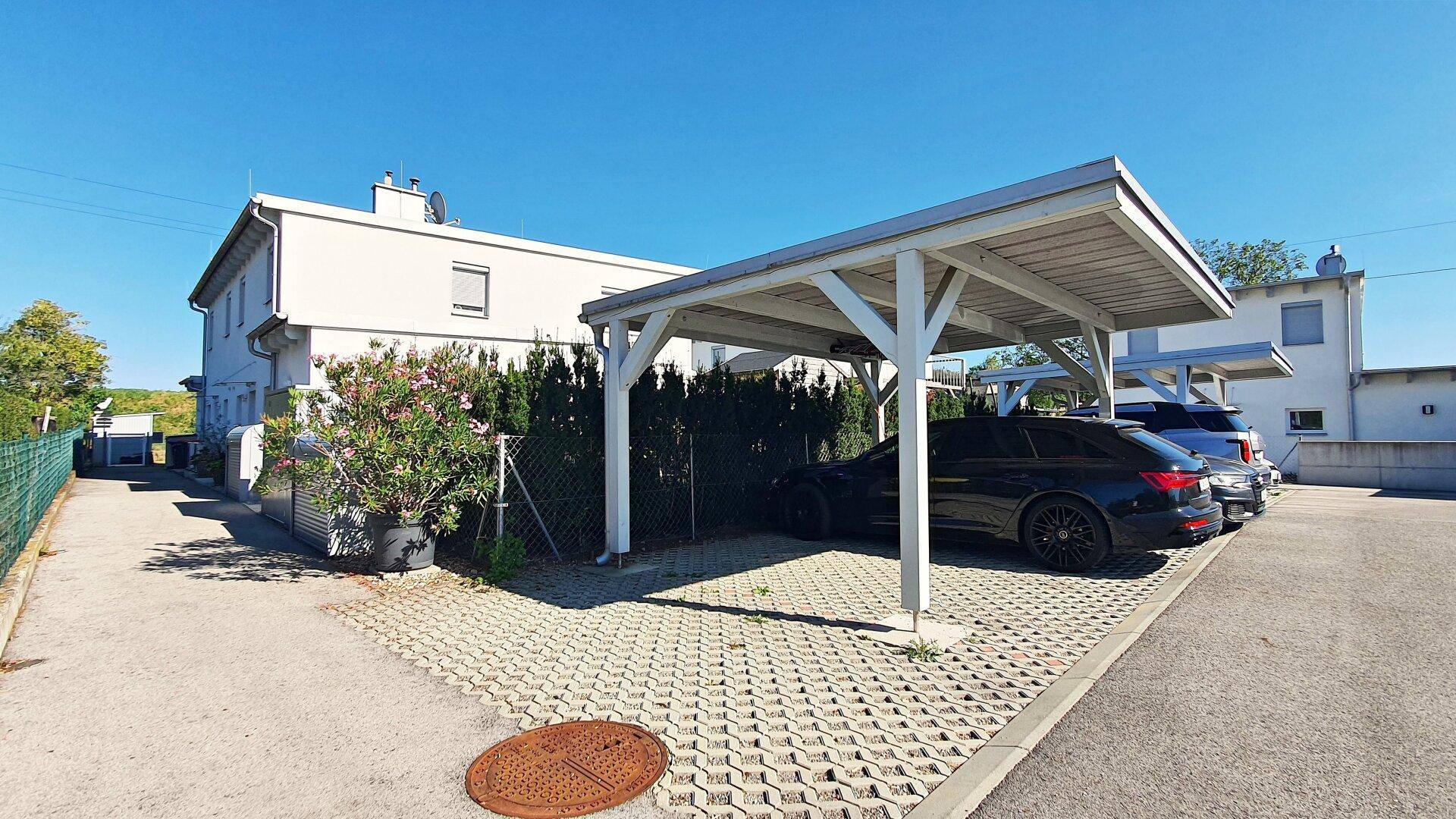 Außenbereich mit Carports und gepflasterten Parkplätzen vor dem Wohnhaus.