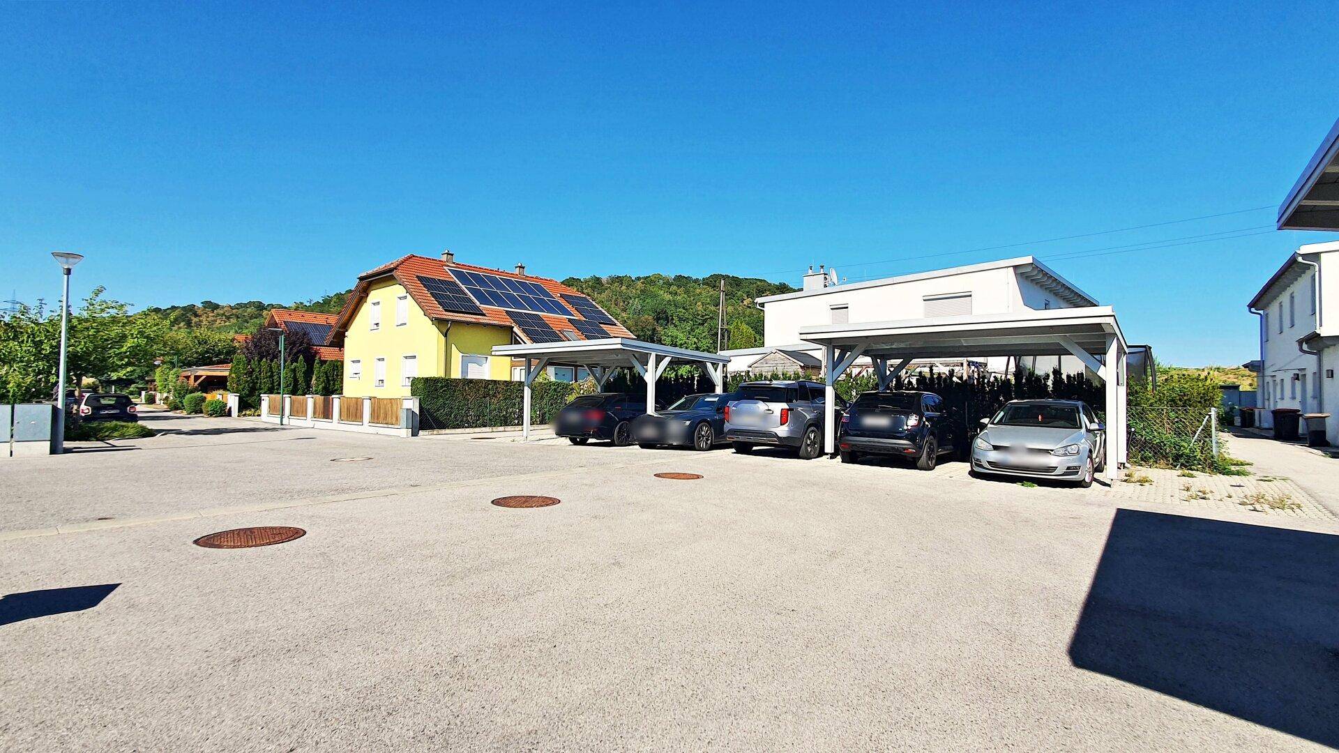 Wohnanlage mit Carports und einem Haus mit Photovoltaikanlage im Hintergrund.