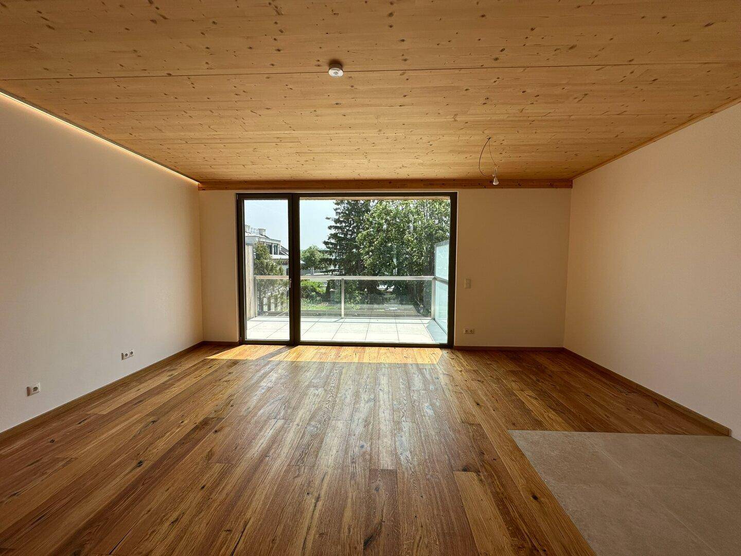 Geräumiger Raum mit Holzboden, Holzdecke und Zugang zu einem Balkon mit viel Tageslicht.