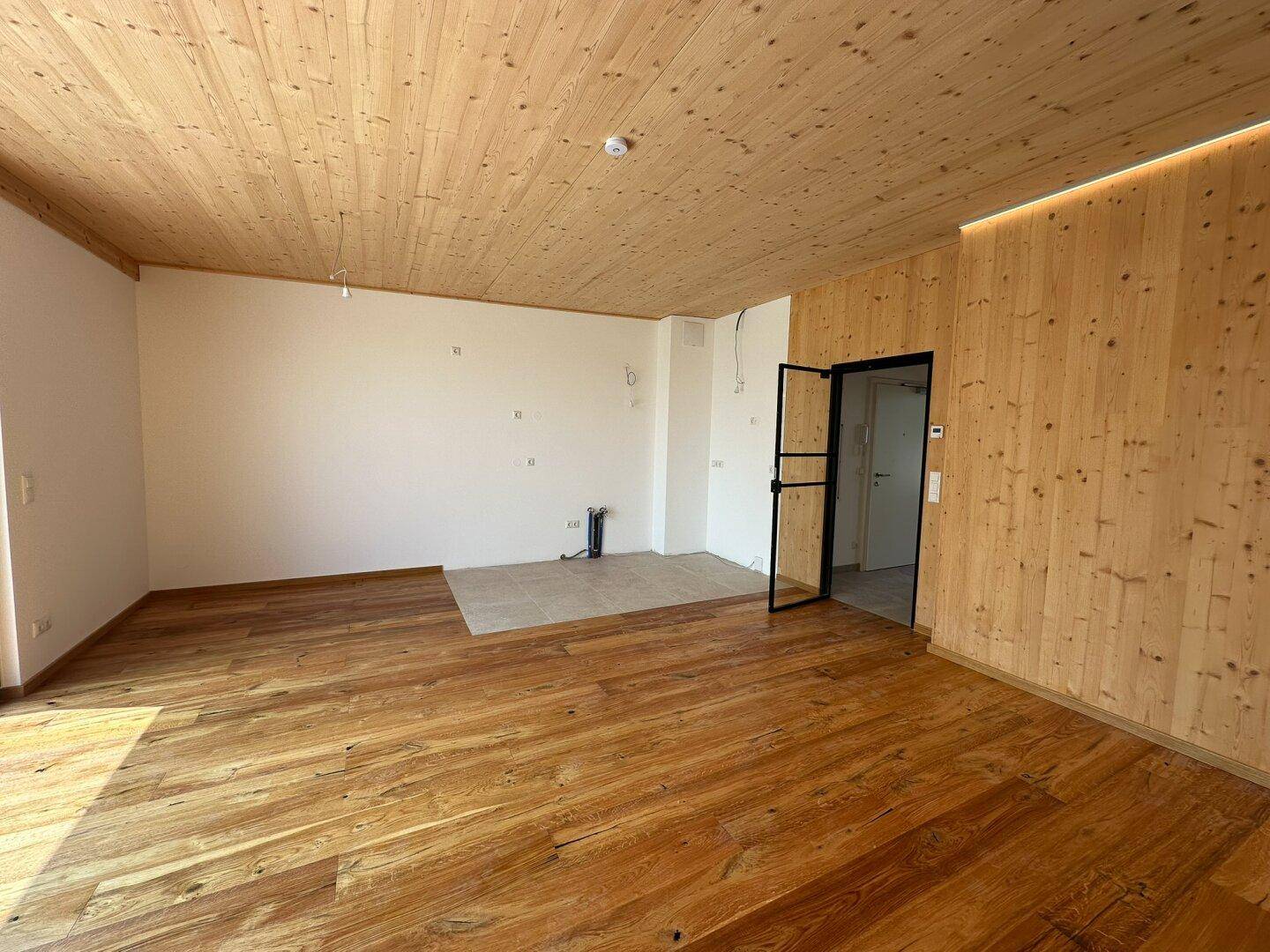 Heller Wohnbereich mit Holzboden, Holzdecke und einer Holzwand mit moderner Beleuchtung.