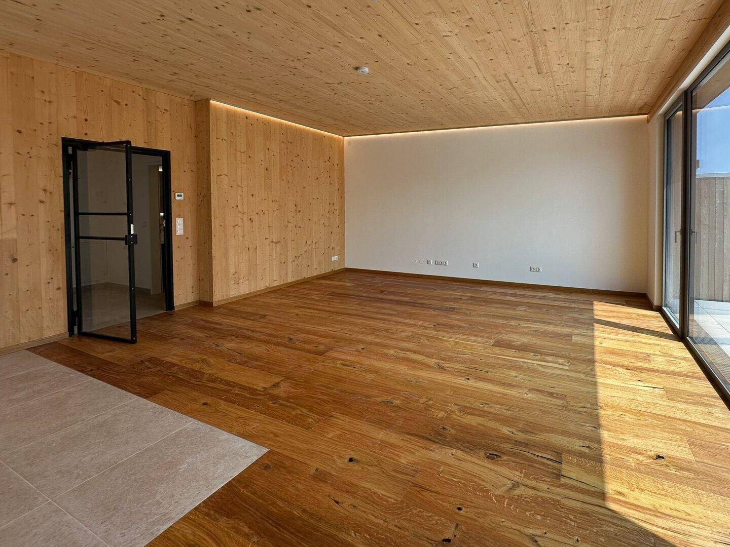 Moderner Wohnraum mit Holzboden, Holzwand und großen Fenstern für viel natürliches Licht.