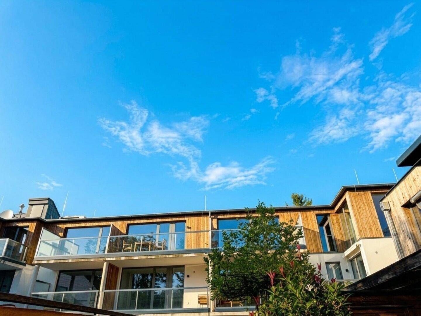 Moderne Architektur mit Holzfassade, großen Glasfronten und Balkonen unter blauem Himmel.