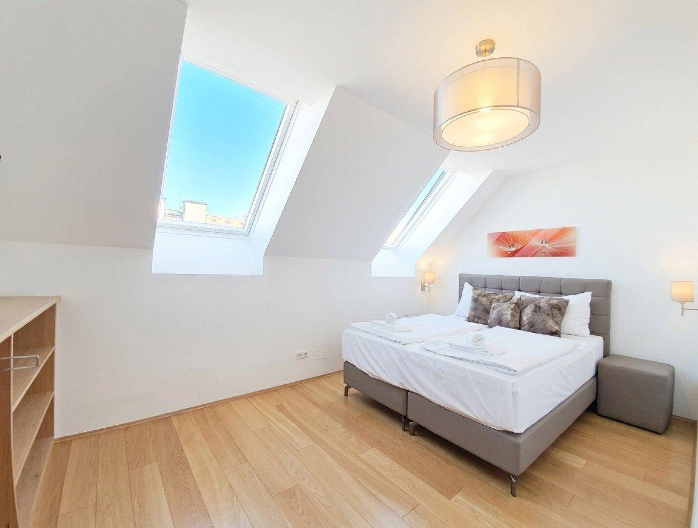 Freundliches Schlafzimmer mit Doppelbett, Holzboden und zwei großen Dachfenstern für eine helle Atmosphäre.
