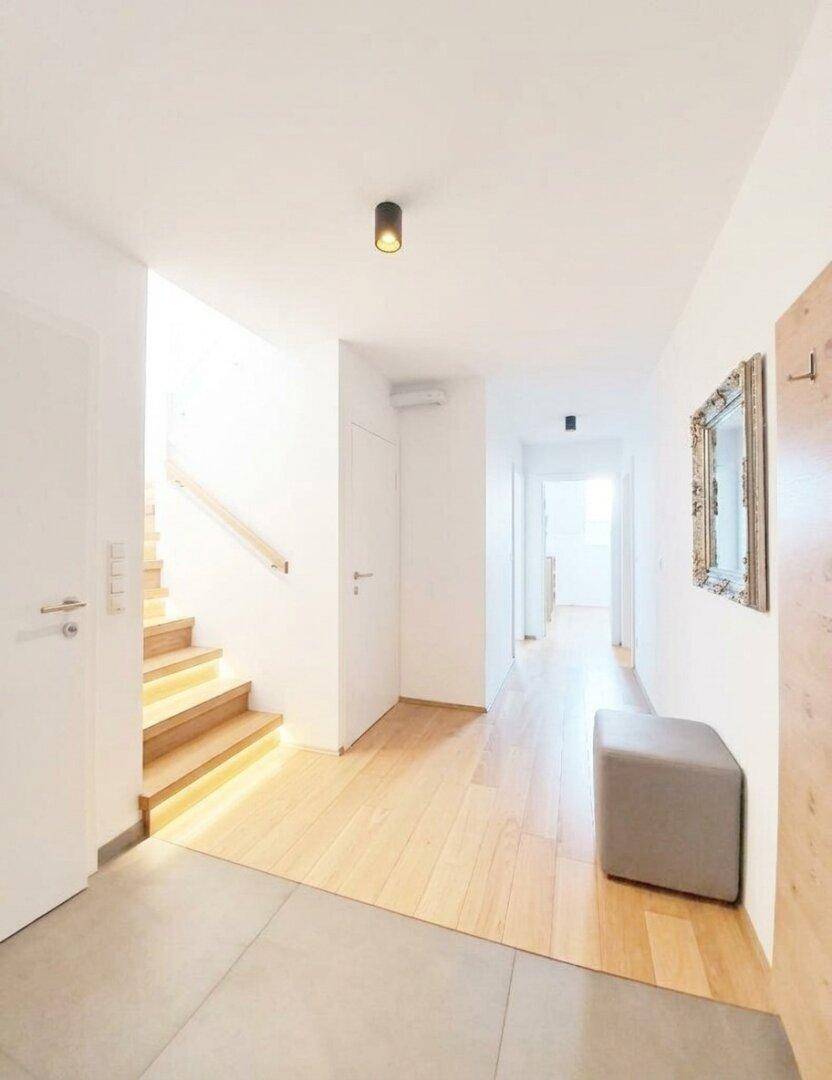 Heller Eingangsbereich mit Holzboden, Fliesenübergang und einer modernen Treppe mit indirekter Beleuchtung.