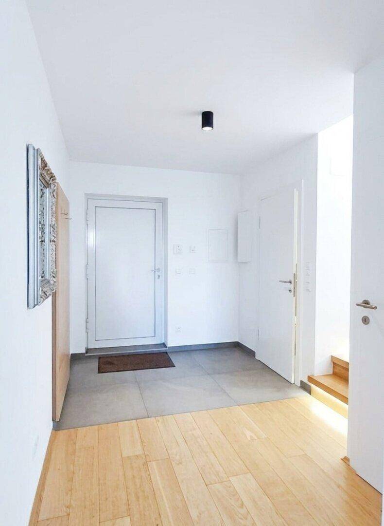 Heller Eingangsbereich mit Fliesenboden, der in einen Holzboden übergeht, und Zugang zur Treppe.