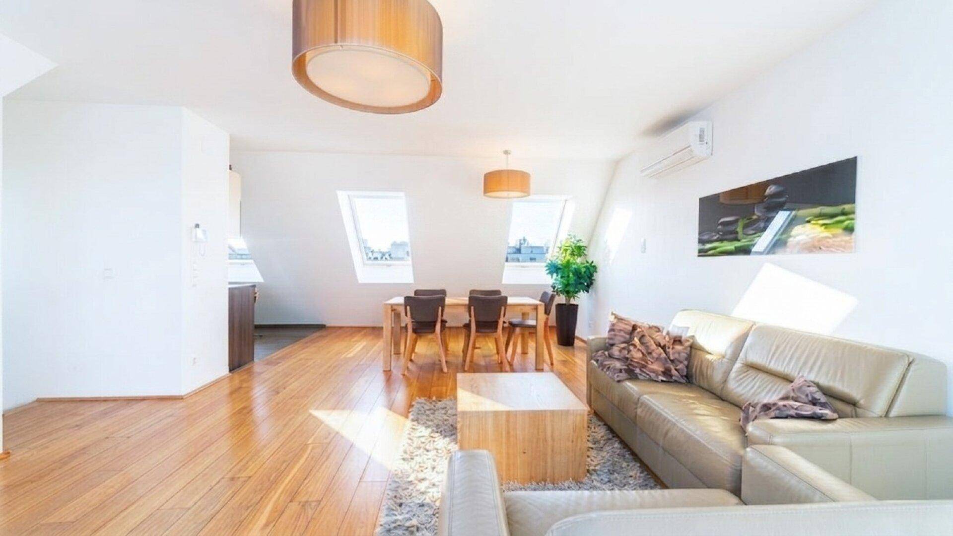Lichtdurchfluteter Wohnbereich mit Holzboden, beiger Couch und Dachfenstern, die viel Helligkeit spenden.