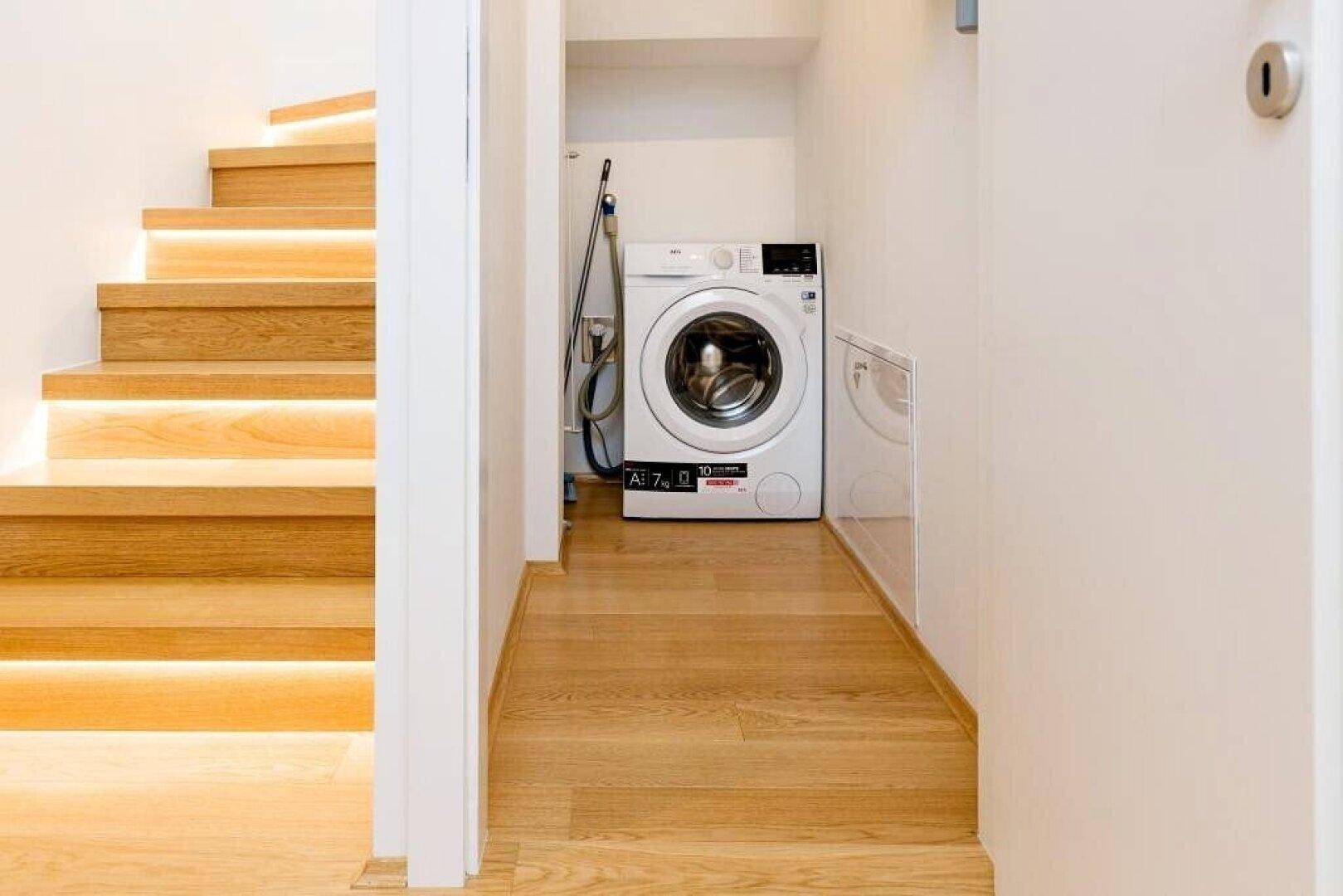 Praktischer Hauswirtschaftsbereich unter der Treppe mit Waschmaschine und Holzboden.
